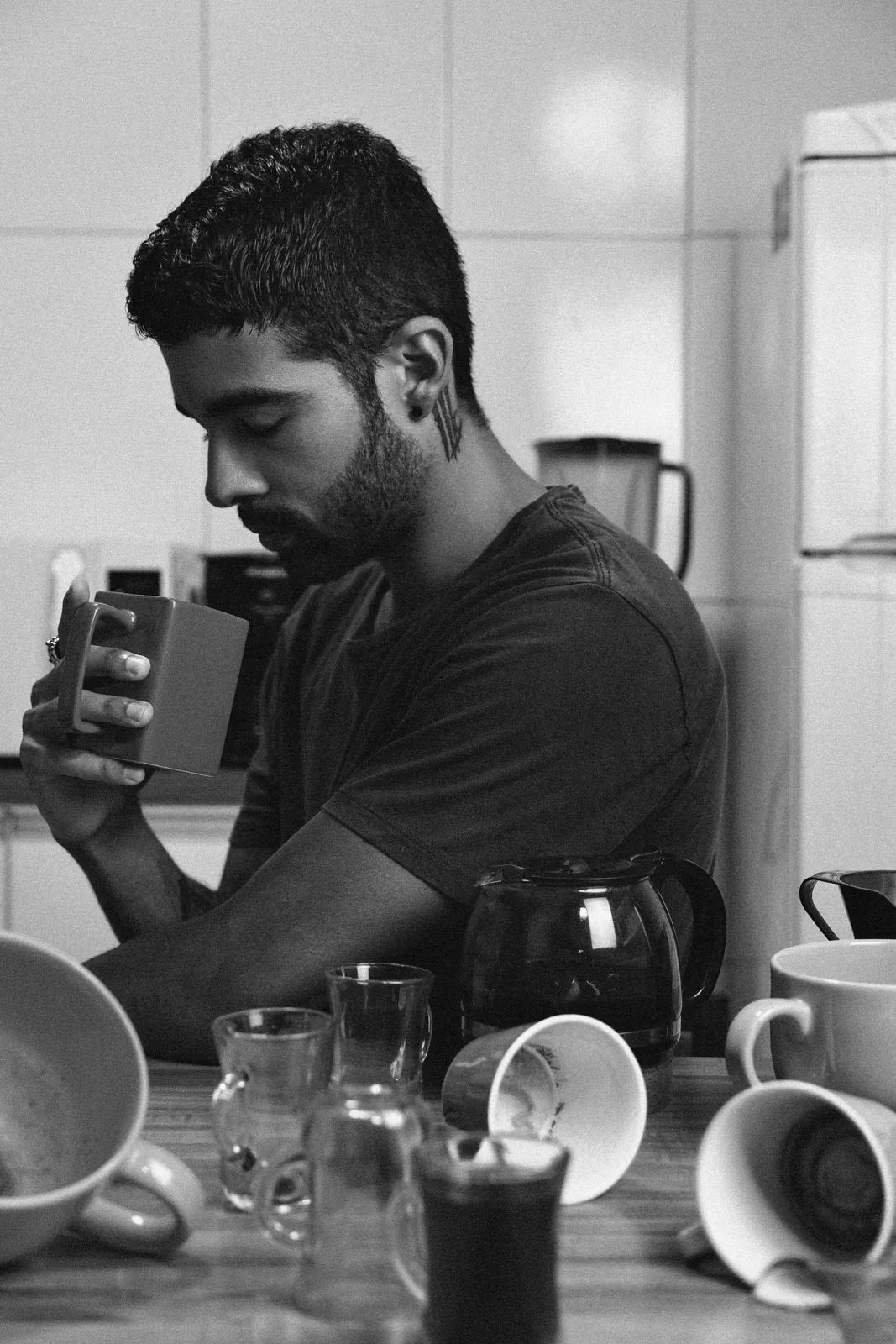 Black-and-white photo of a tired man sitting in a kitchen, holding a coffee mug