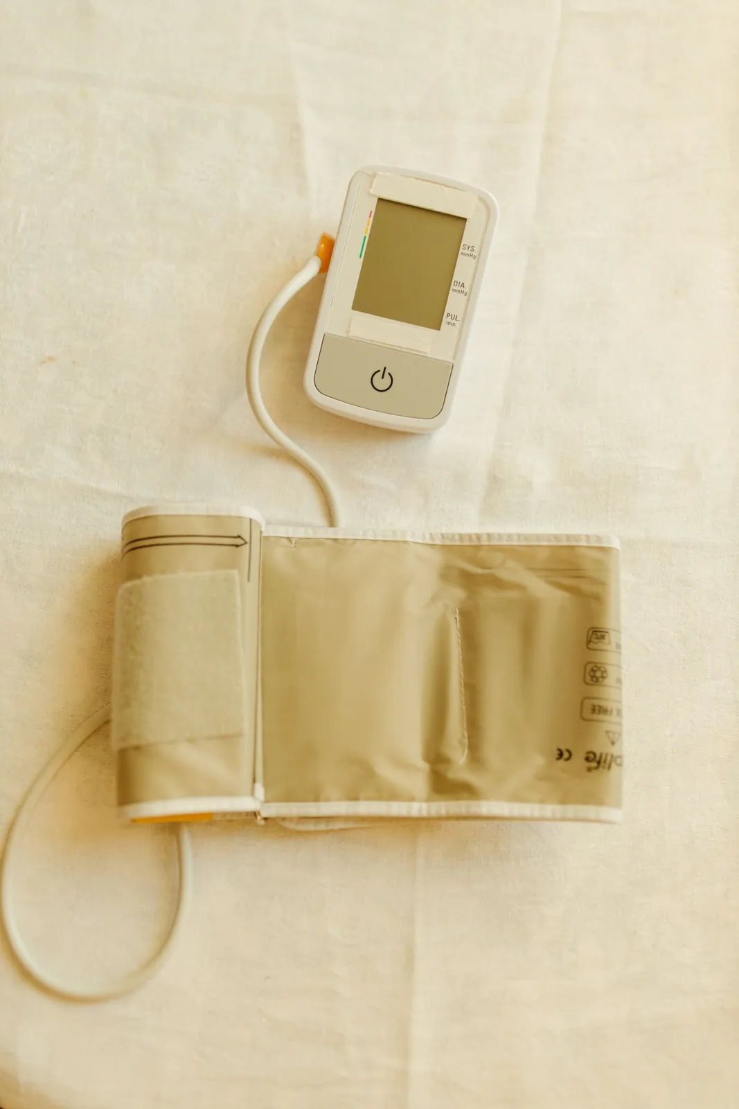 A digital blood pressure monitor and arm cuff on a white cloth, seen from above