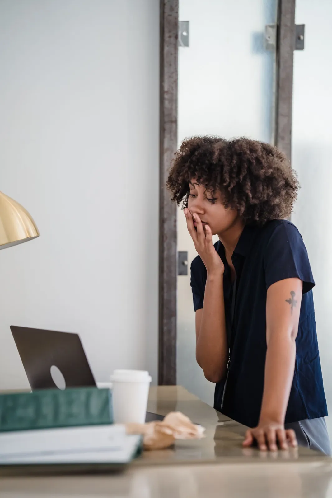 A young woman yawning while she works on a laptop at a home desk