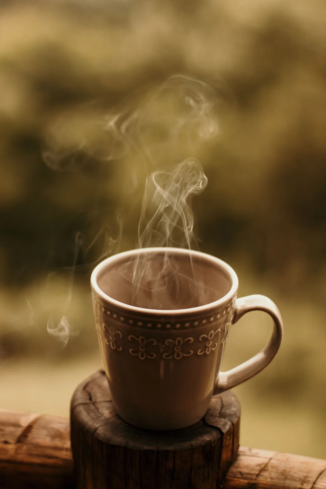 A steaming mug of coffee on a wooden coaster outdoors