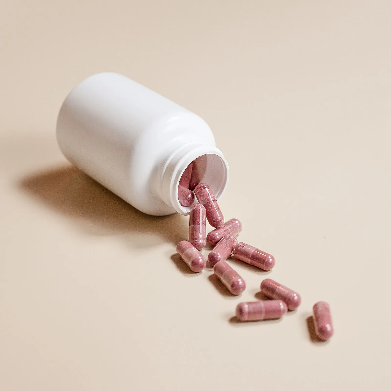 A white pill bottle spilling pink capsules onto a beige surface
