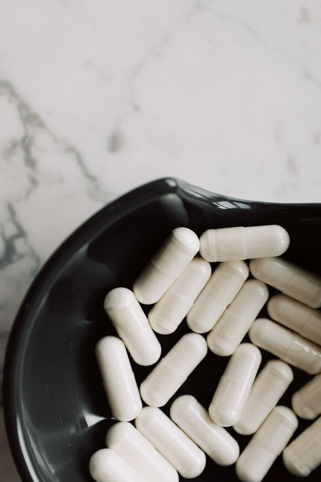 White capsules in a black bowl on a marble counter