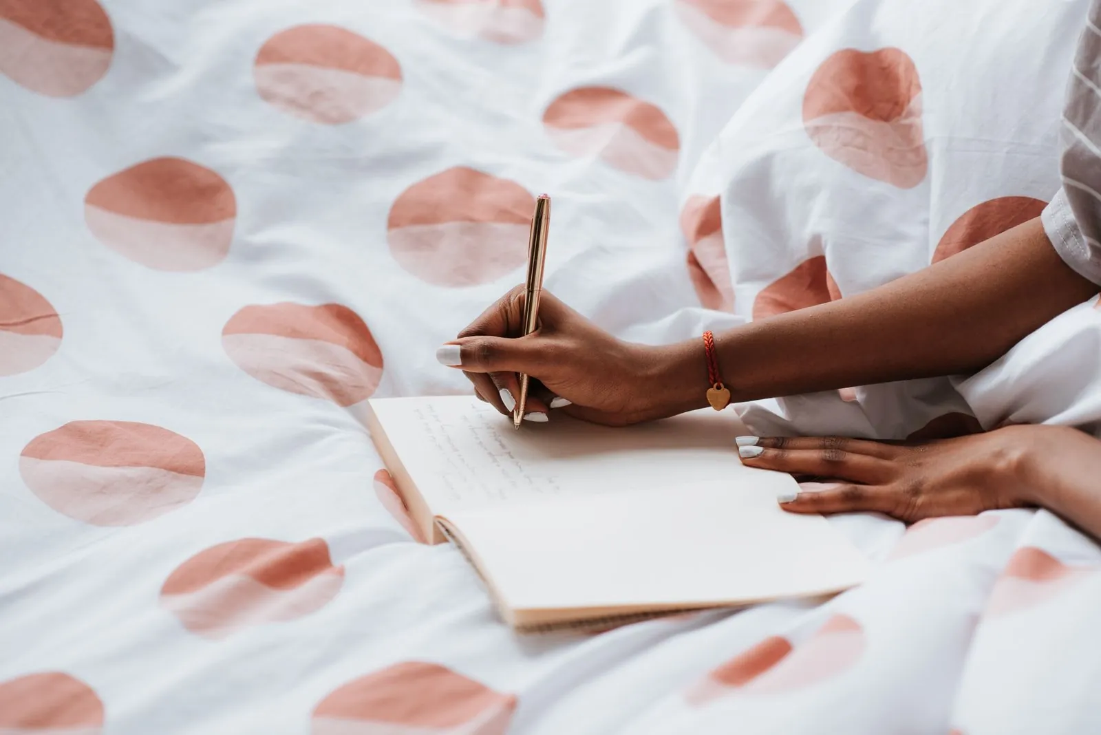 A woman writing in a notebook on a bed with polka-dot sheets