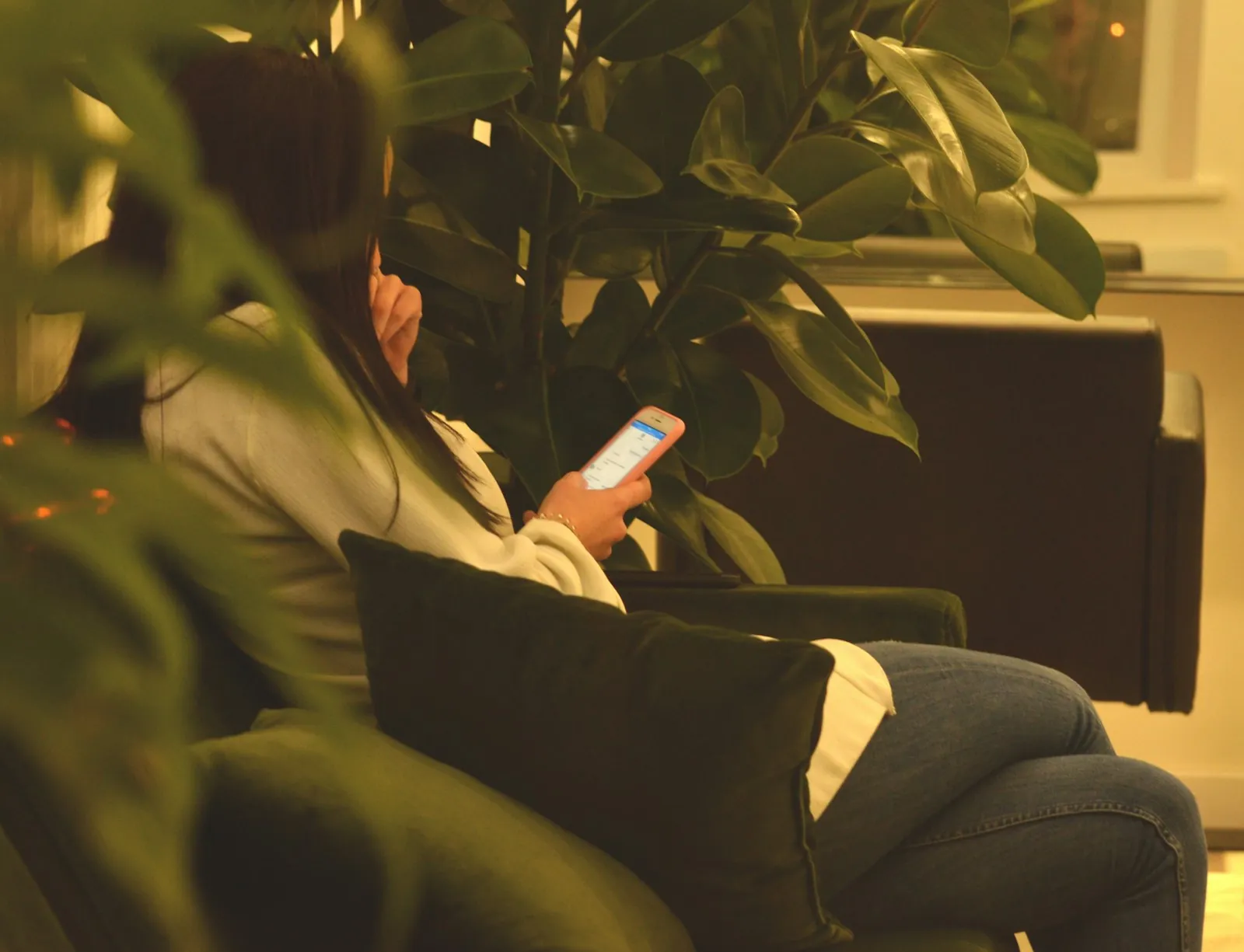 A woman using her smartphone on a sofa between green plants