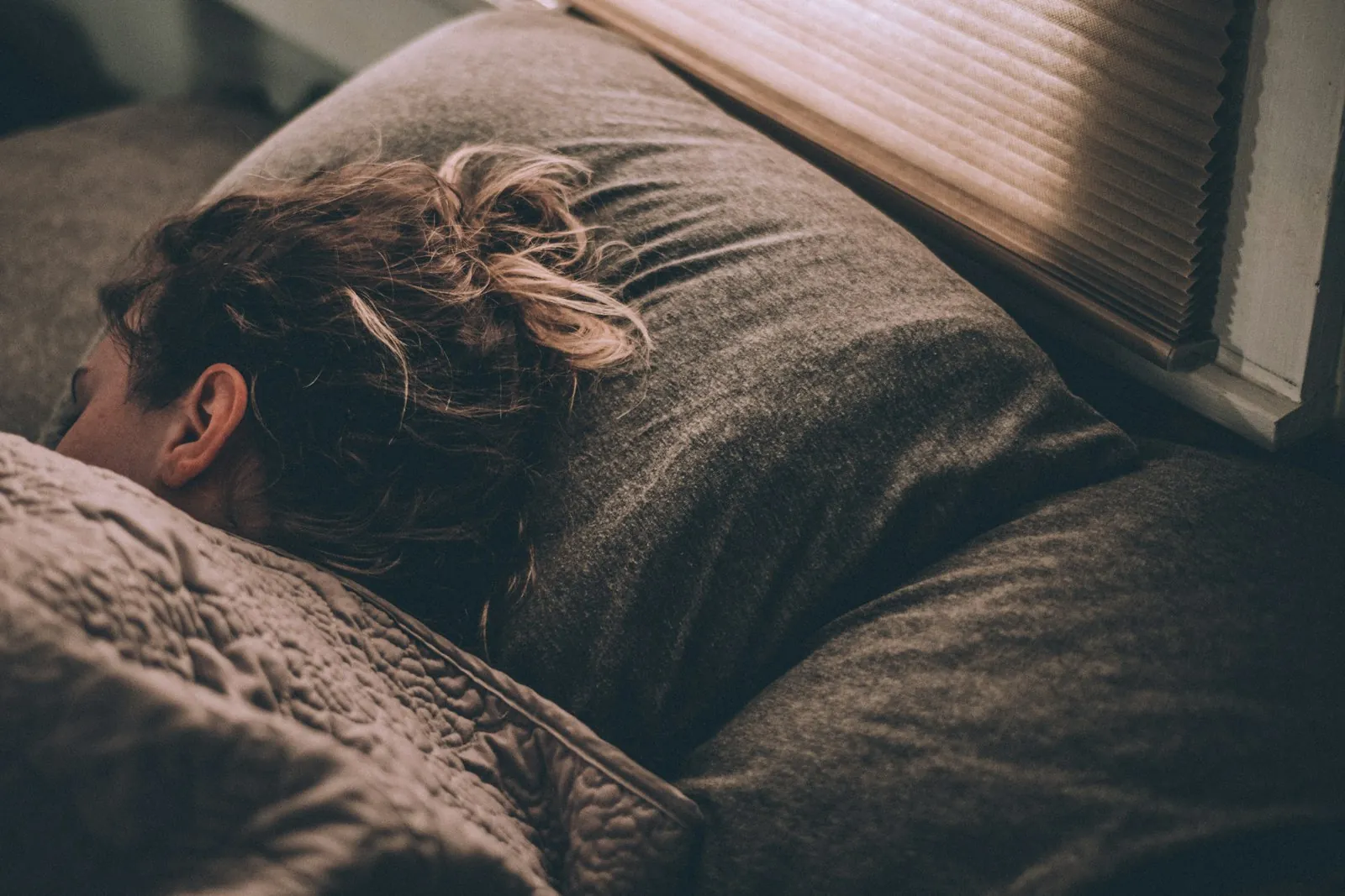 A woman asleep in bed under blankets in morning light