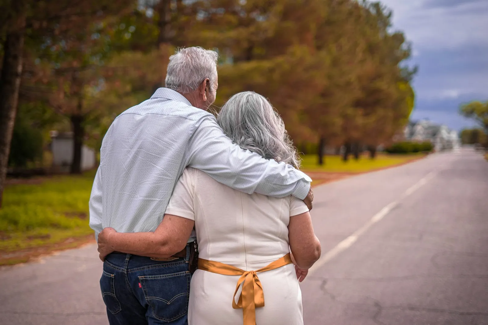 An older man and woman with gray hair walking arm in arm down a road