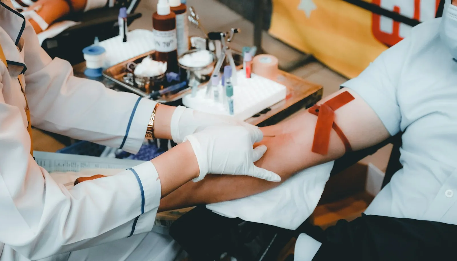 Healthcare worker in white gloves drawing blood from a person's arm with a needle and collection tube