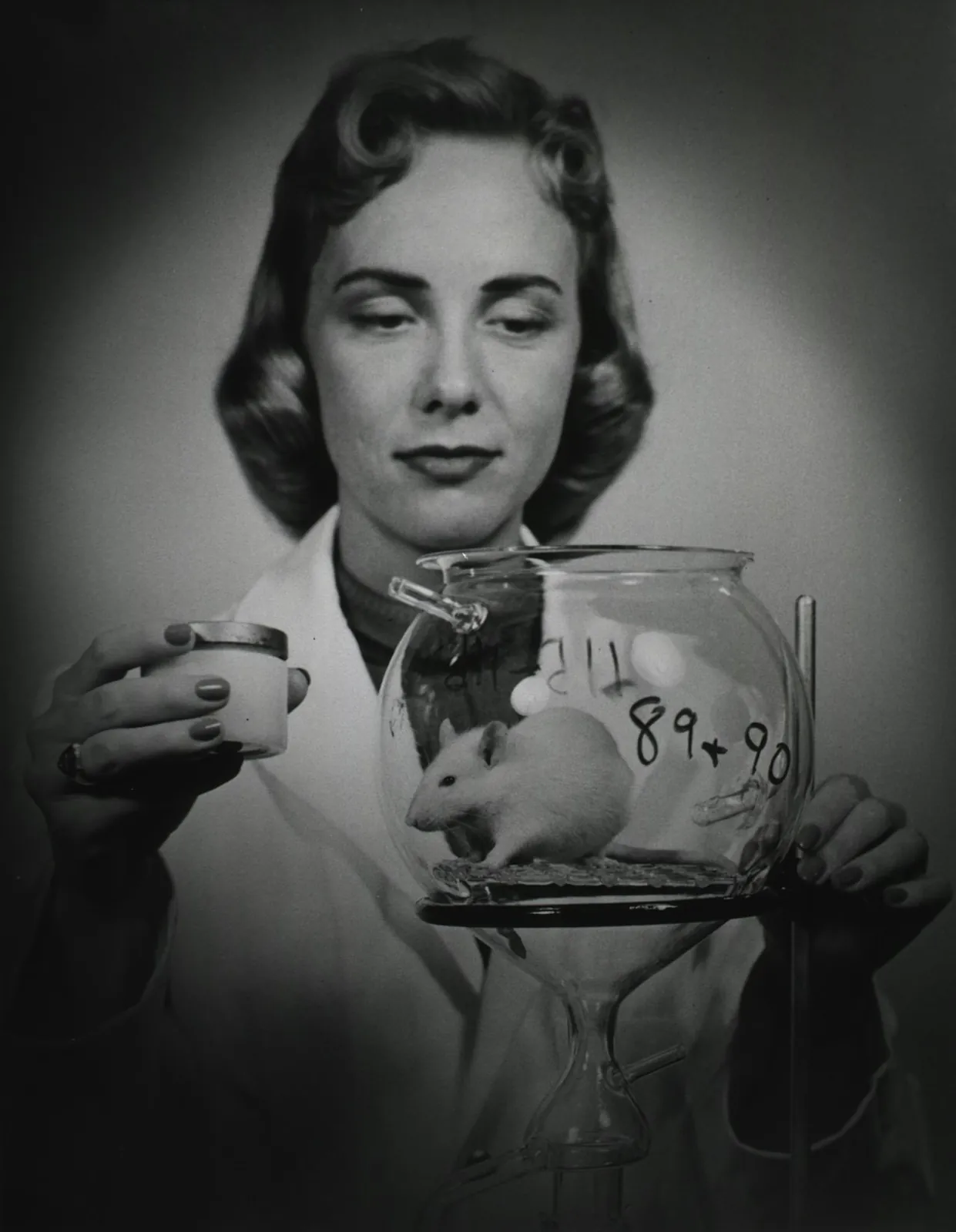 A scientist holds up a glass jar with a lab mouse inside