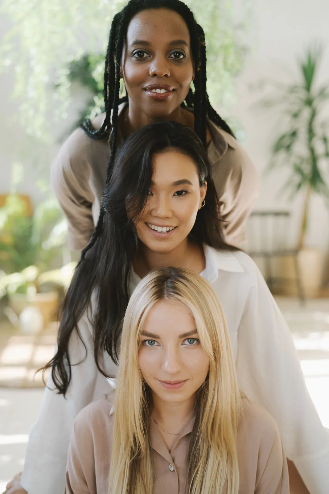 Three smiling women with different skin tones standing close together indoors