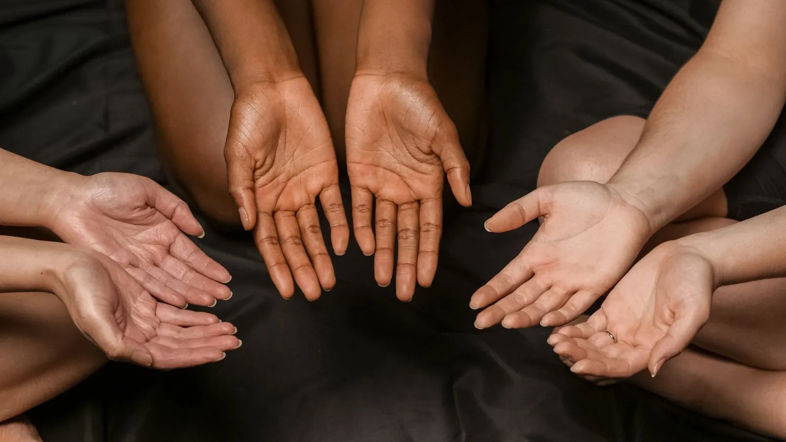Hands with many different skin tones arranged in a circle on a dark surface