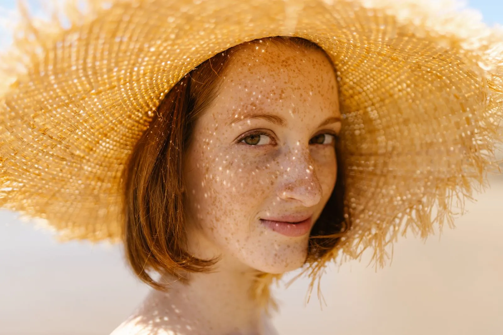 A smiling woman with freckles wearing a straw sun hat outdoors