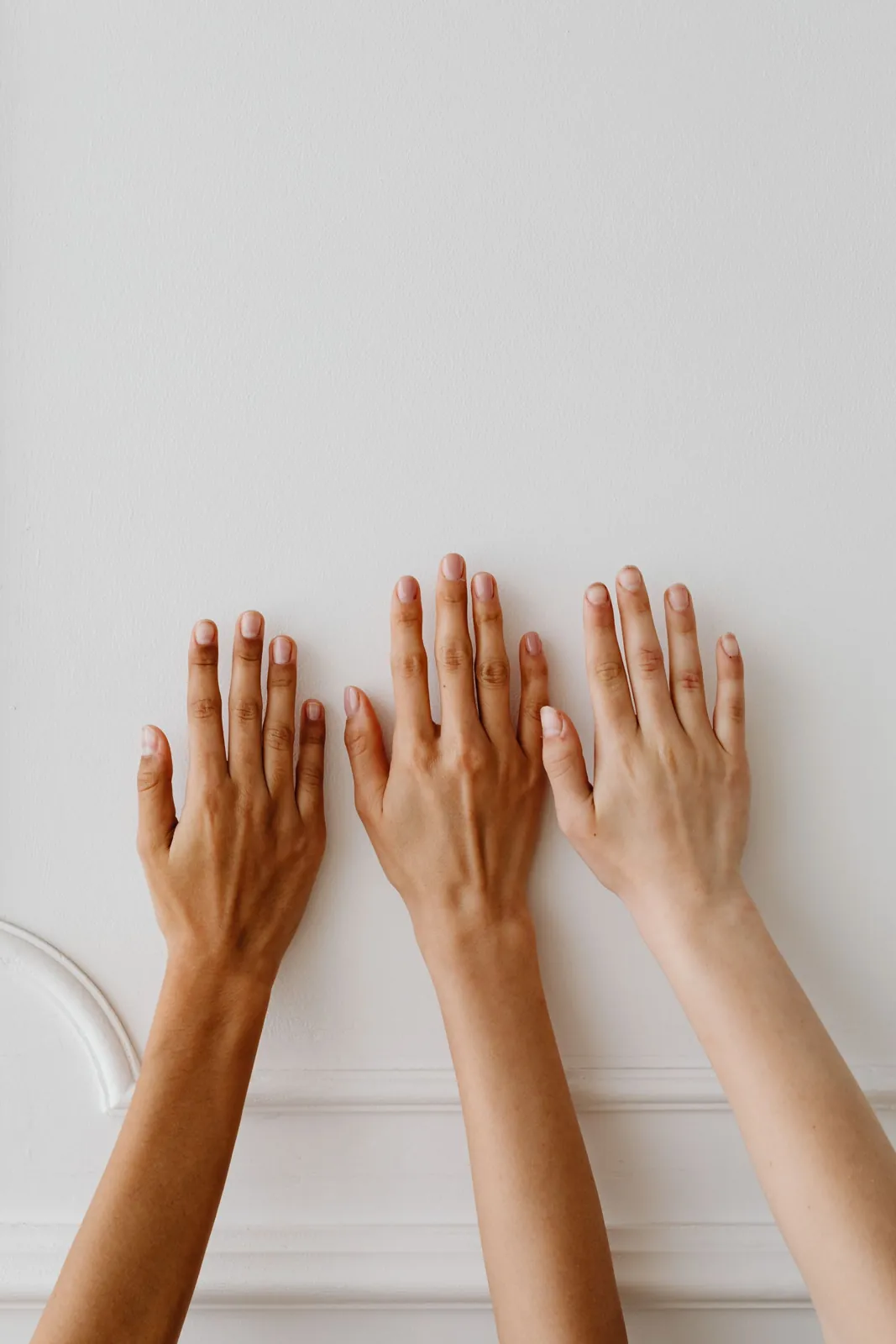 Three hands with different skin tones pressed against a white wall