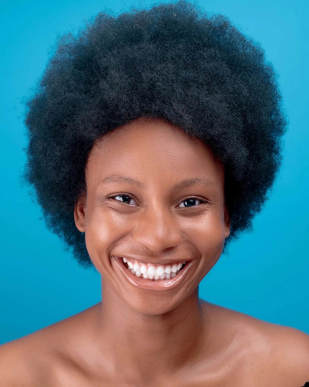 A smiling woman with black curly hair in an afro against a blue background