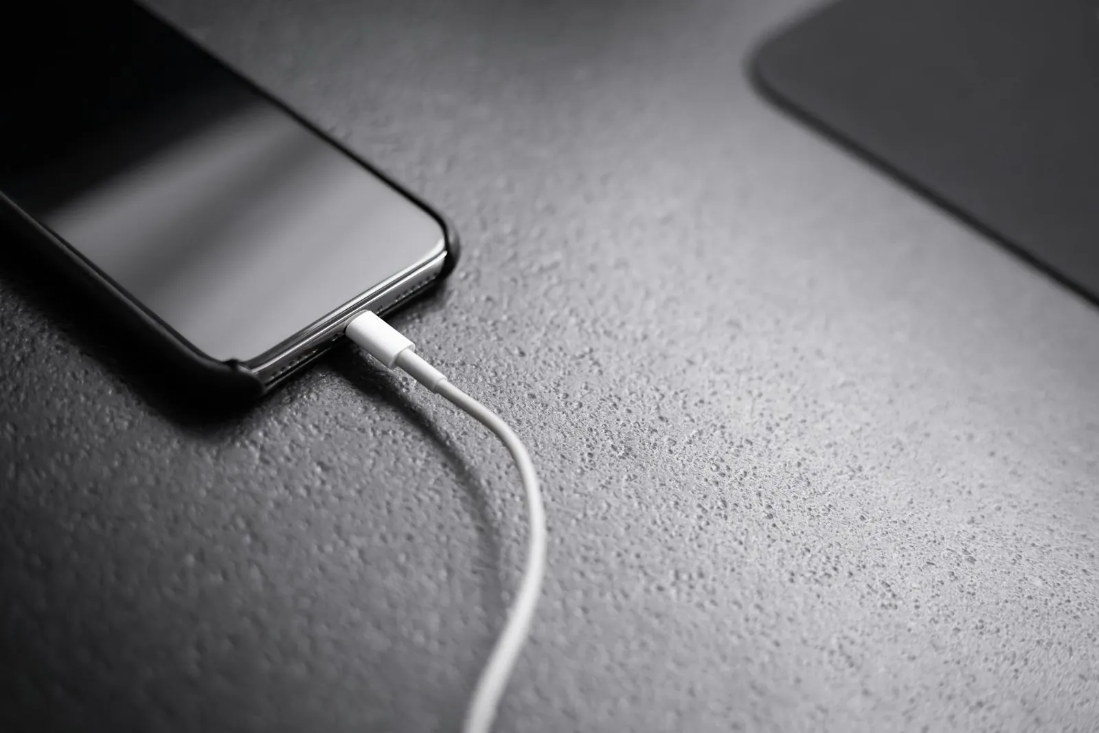 A black smartphone plugged into a charging cord on a table