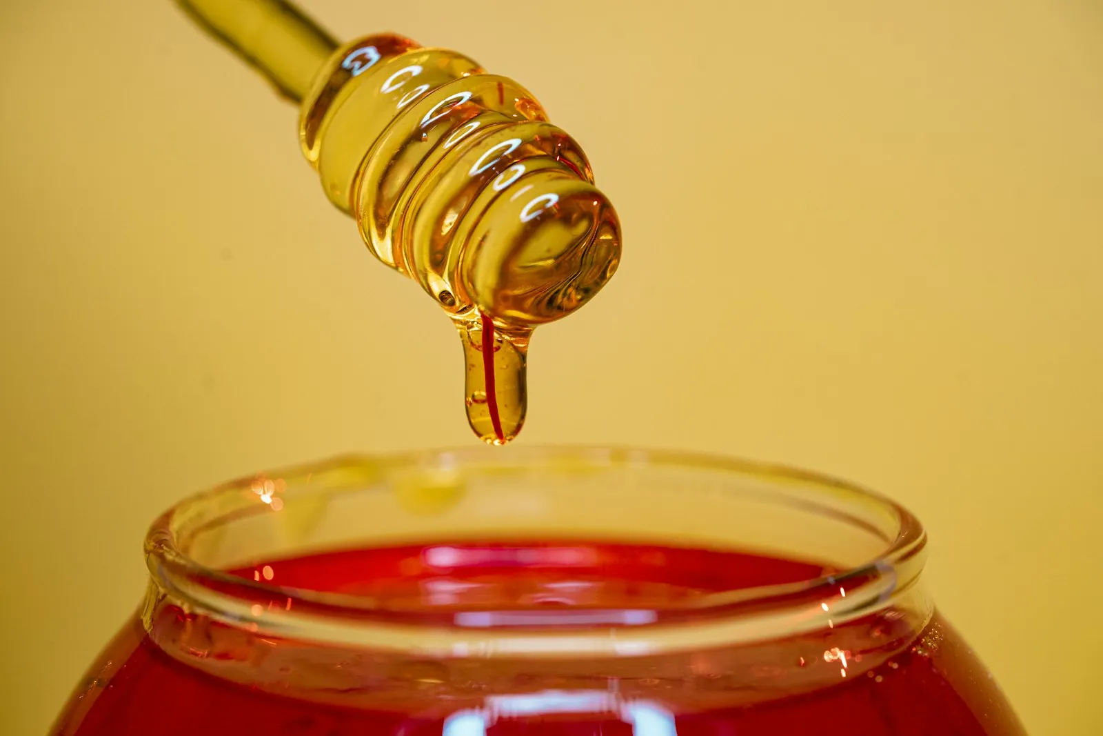 Golden honey dripping from a wooden dipper into a glass jar