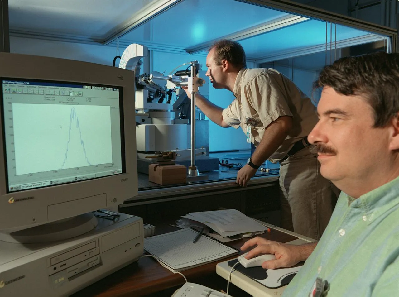 Two NASA scientists check a protein crystal on a diffractometer, a machine that aims X-rays at crystals