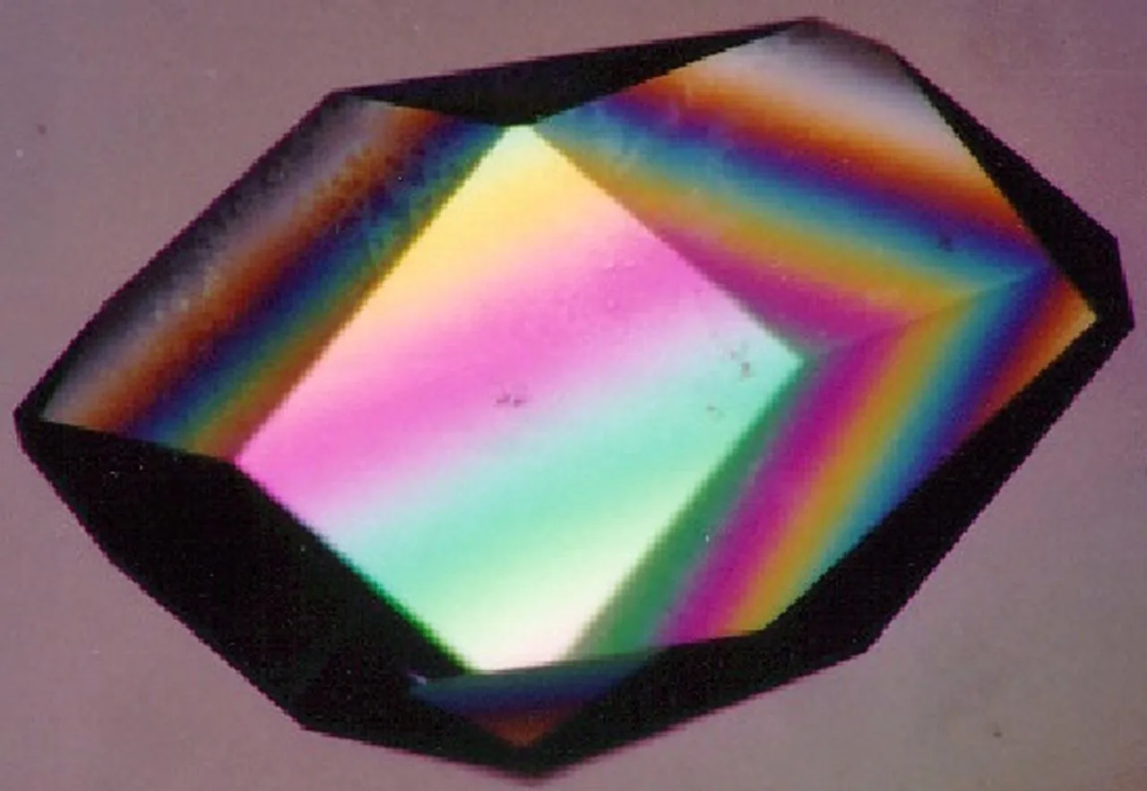 A lysozyme protein crystal grown in space, glowing in rainbow colors under polarized light