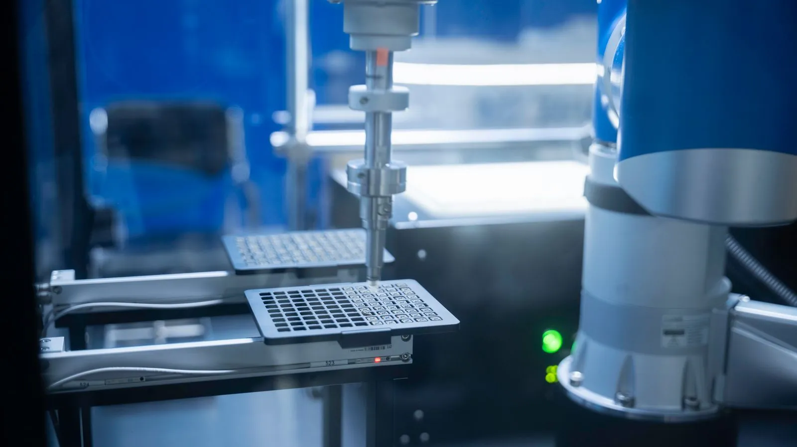 A lab robot arm moves plates that hold hundreds of tiny wells