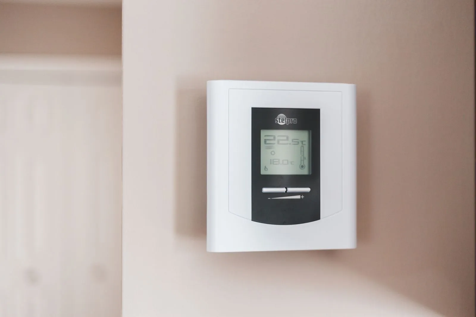A digital thermostat on a wall, showing a temperature setting in Celsius