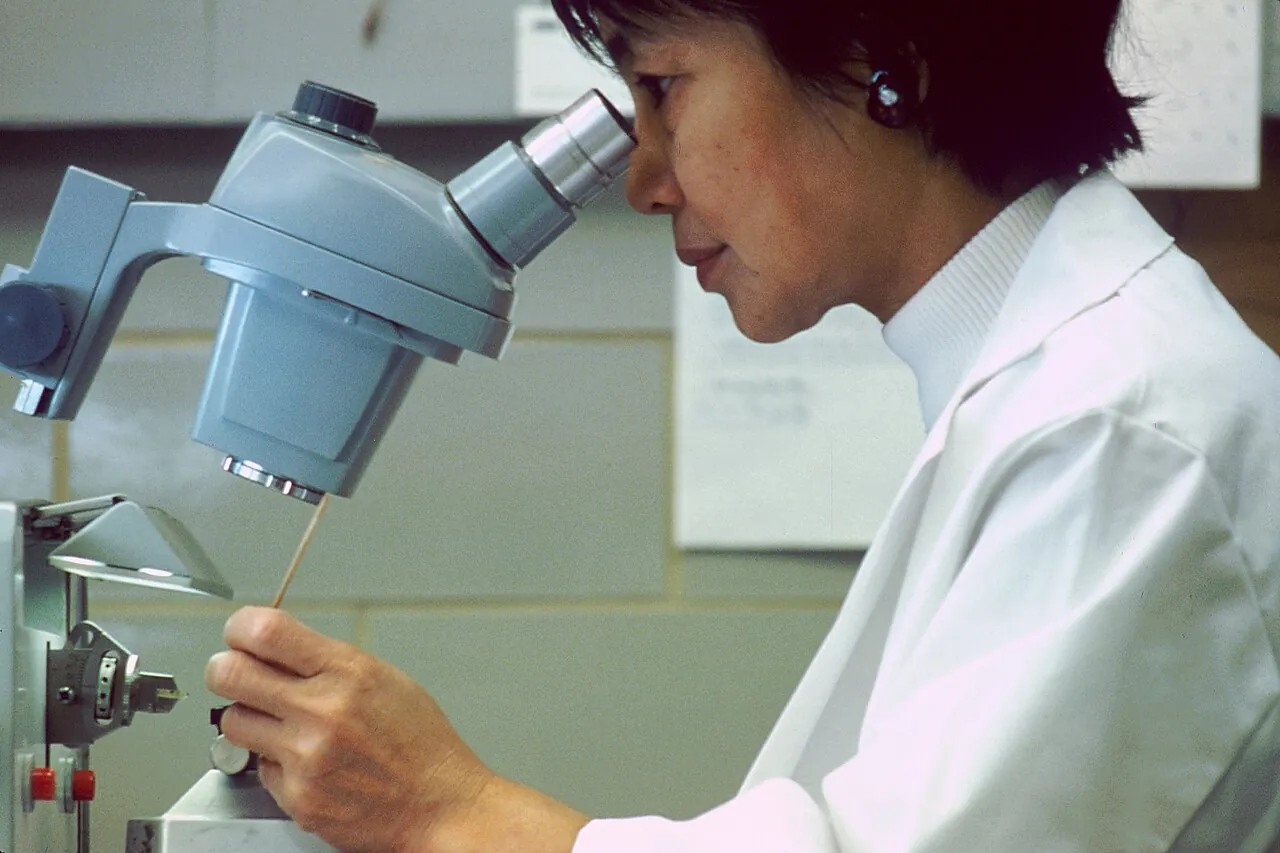 A scientist in a lab coat looking through a microscope