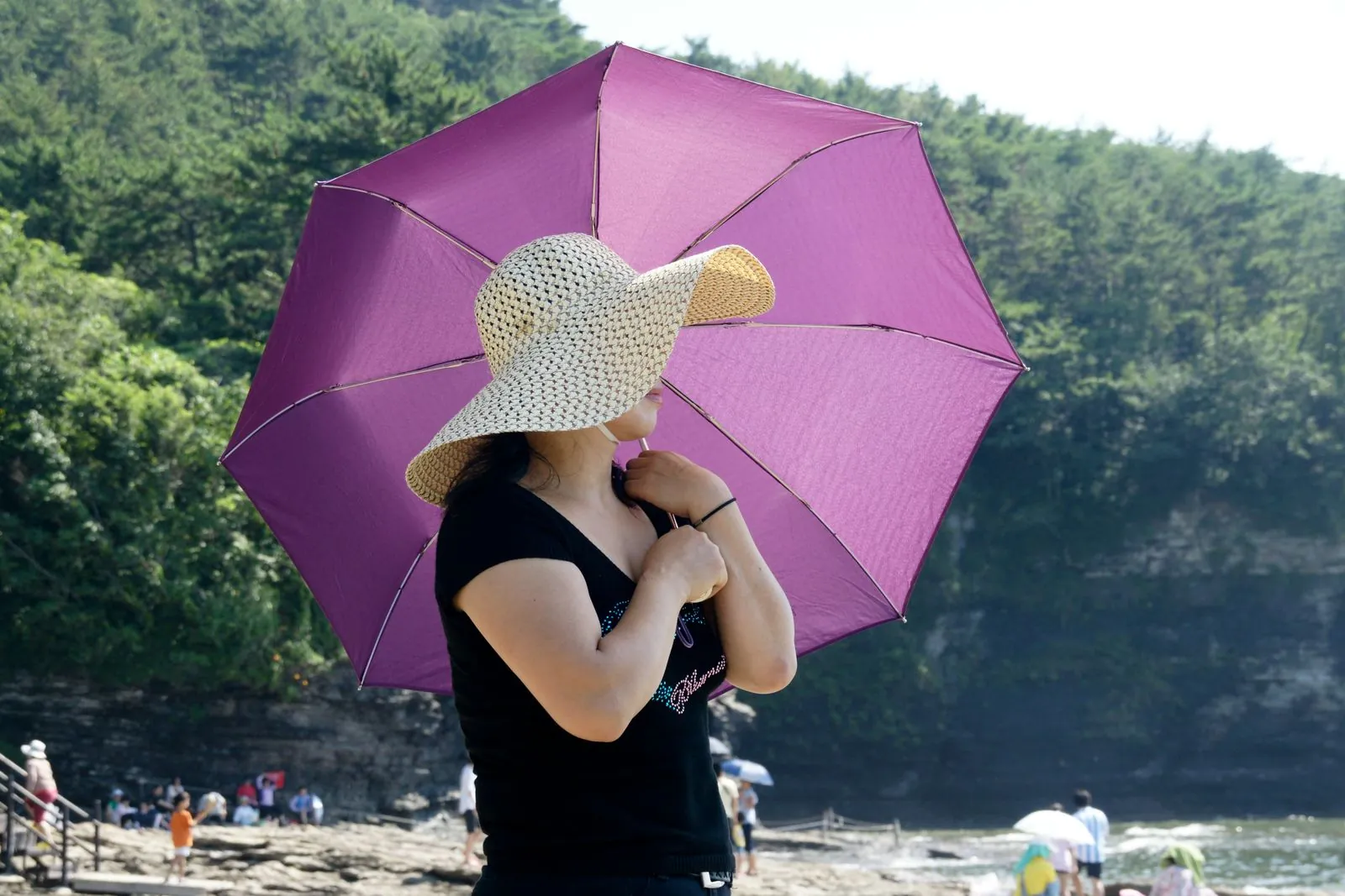 A woman in a sun hat holding a pink umbrella on a sunny beach