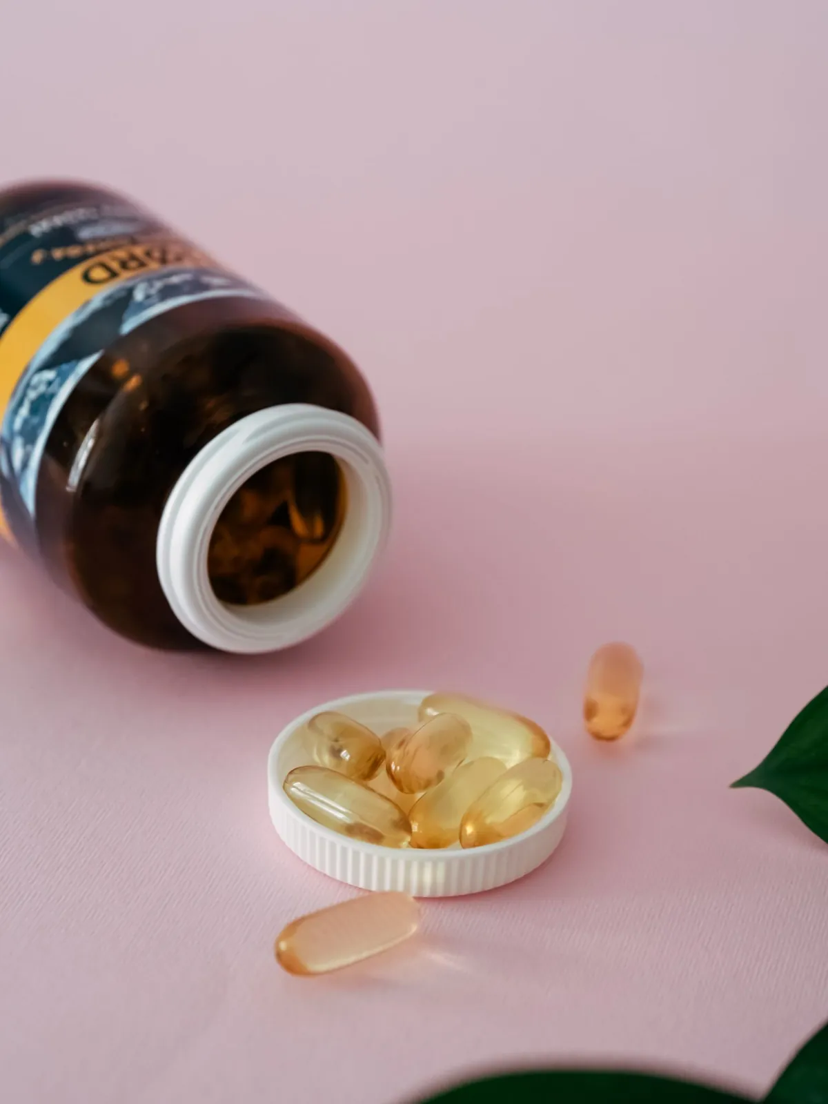 Cod liver oil capsules and a small bottle on a pink background