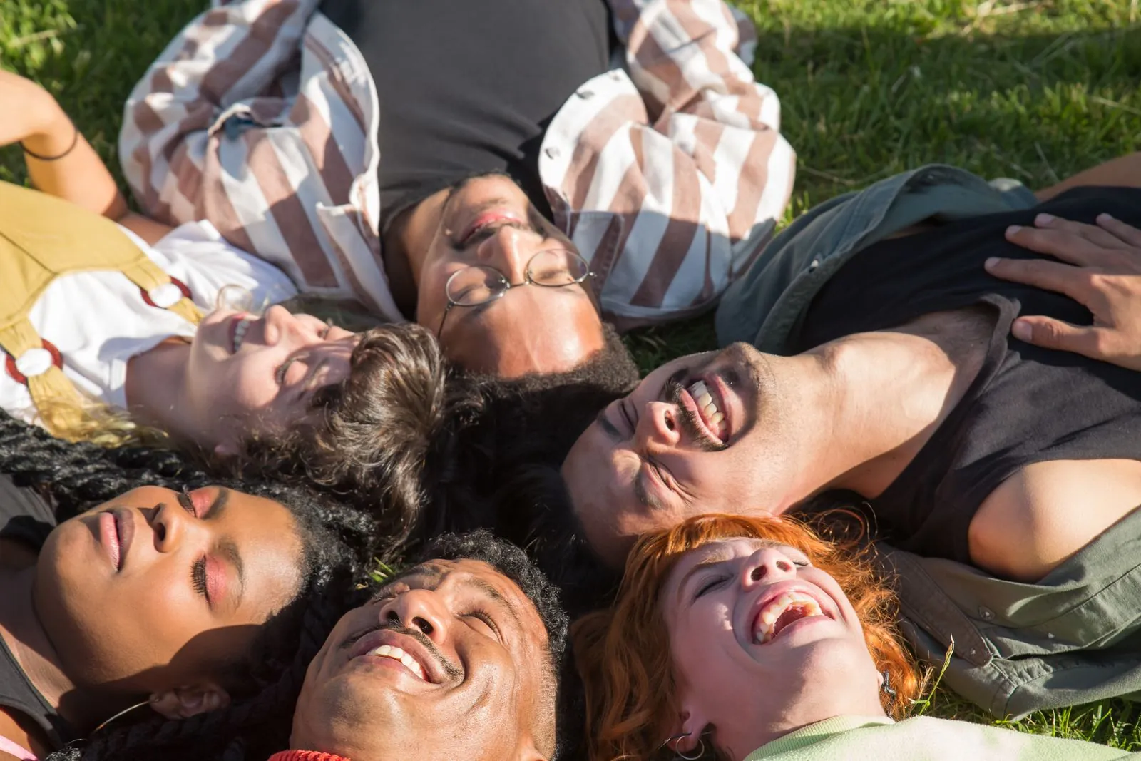 A group of friends with a range of skin tones lying on the grass and laughing under a sunny sky