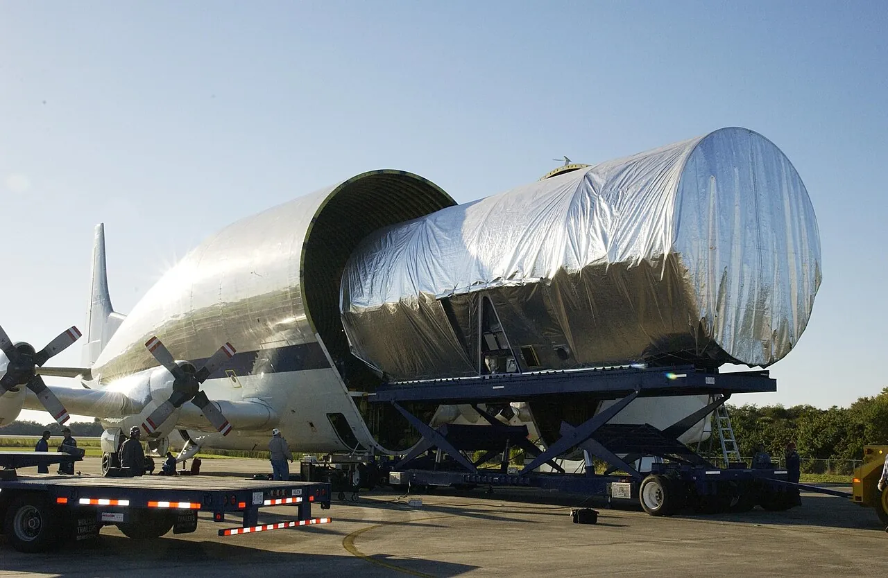 A long piece of space station truss rolls out of the Super Guppy's open nose at Kennedy Space Center