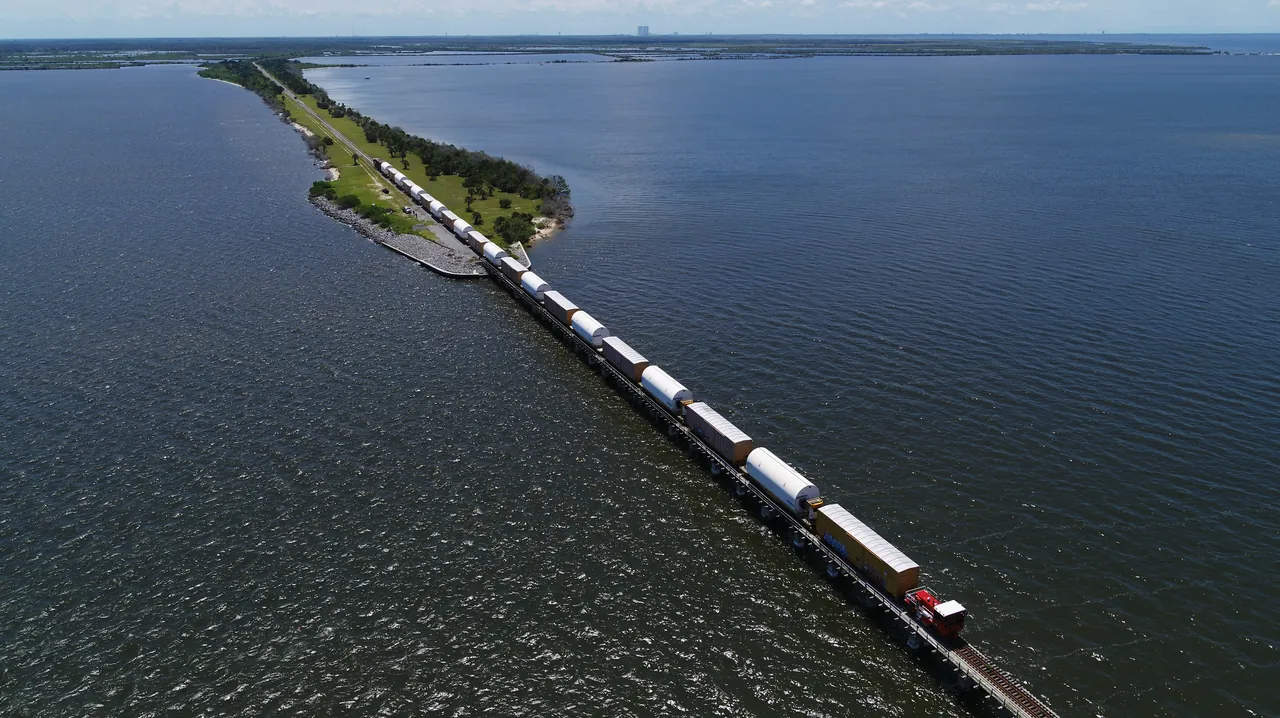 Railcars carry Space Launch System booster segments across a causeway toward NASA's Kennedy Space Center