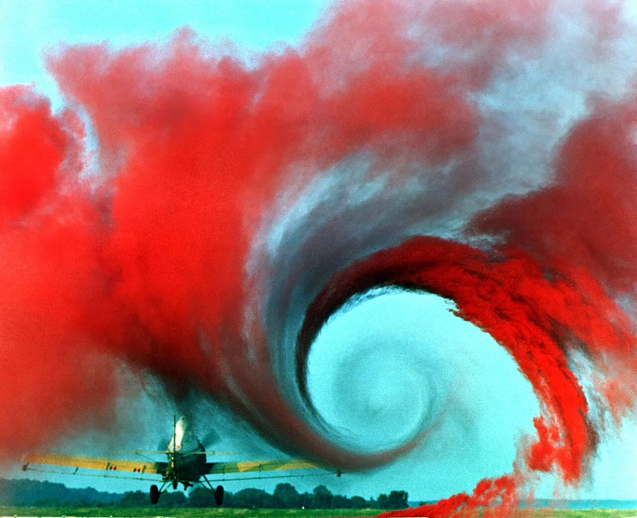 Colored smoke curls into a spinning spiral of air behind the wingtip of a small plane during a NASA air flow test